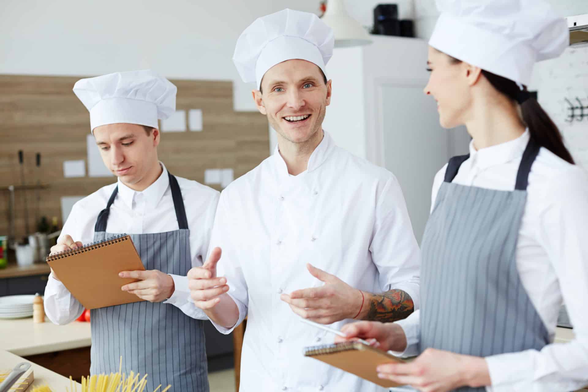 Consulting trainees Happy young chef giving advice to his trainees during process of cooking