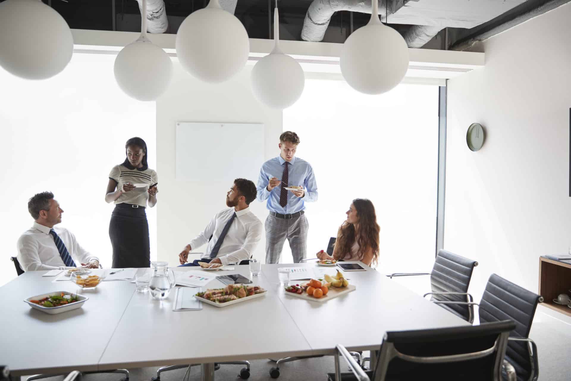 Businessmen And Businesswomen Meeting In Modern Boardroom Over Working Lunch Businessmen And Businesswomen Meeting In Modern Boardroom Over Working Lunch