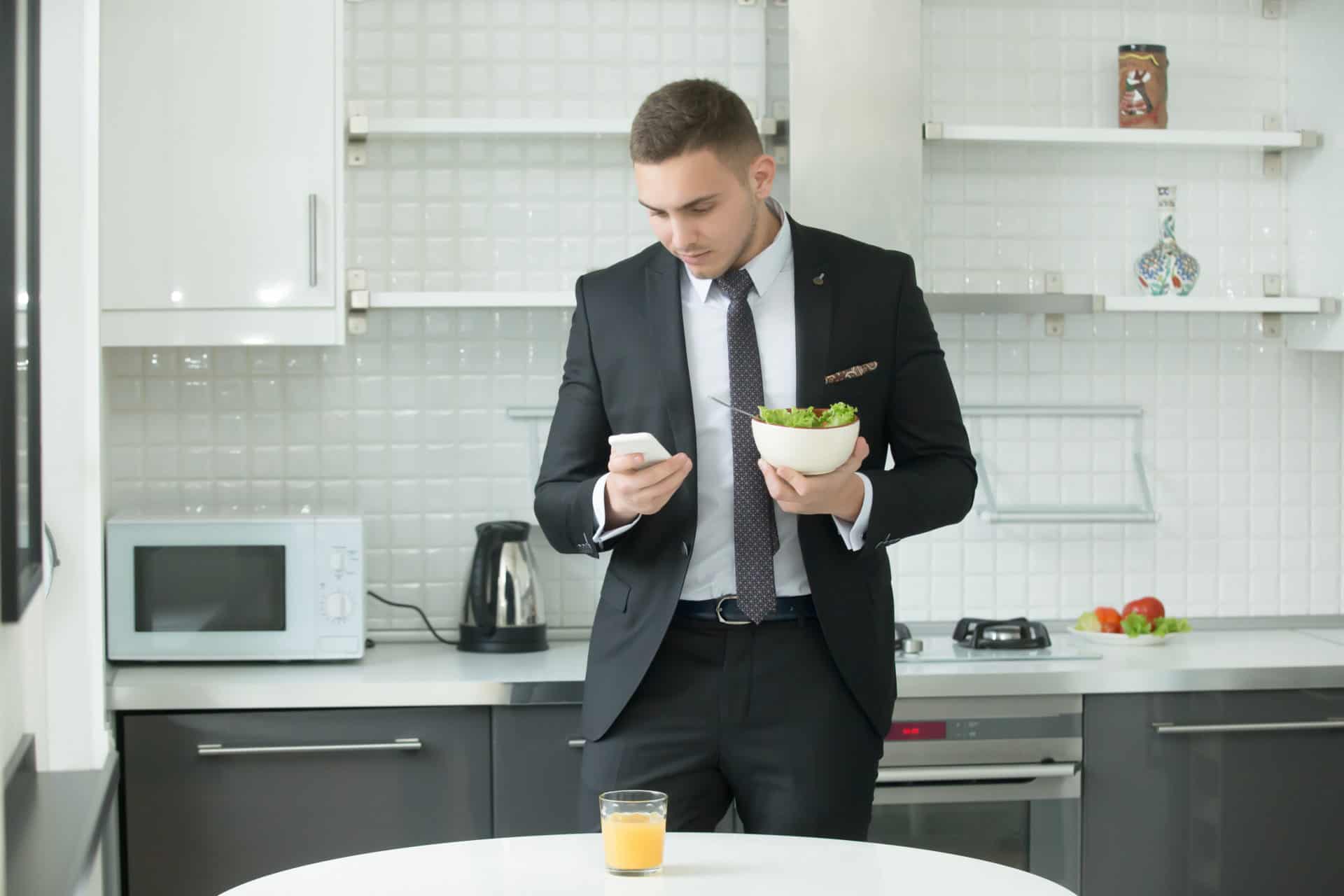 Young handsome businessman having lunch Businessman at the modern kitchen having vegan lunch, looking at his smartphone