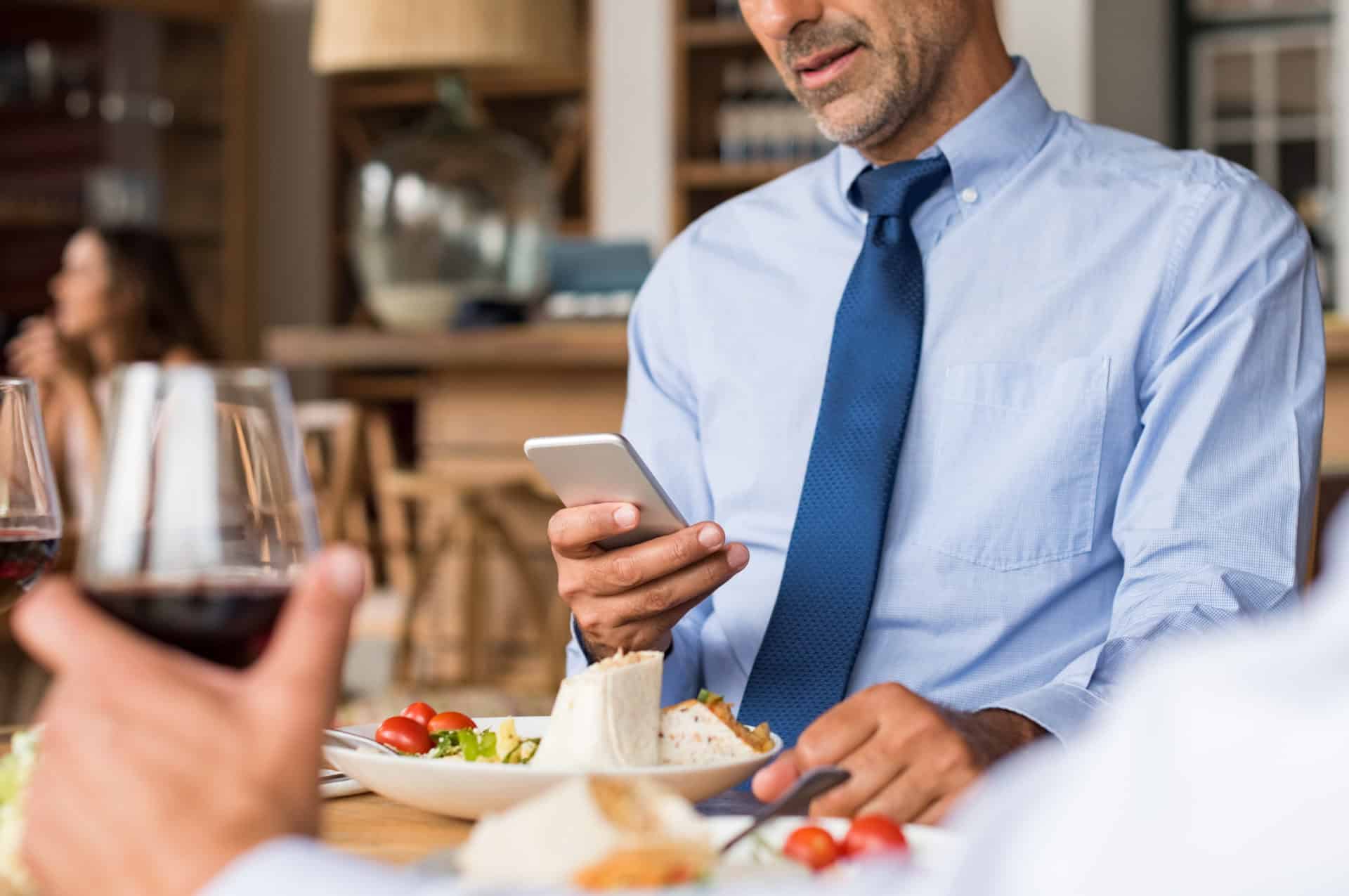 Businessman using phone Hands of a businessman using phone at restaurant during business lunch. Closeup of a man hand reading email on phone while having lunch in cafe. Businessman sending message and updating team after a meeting.